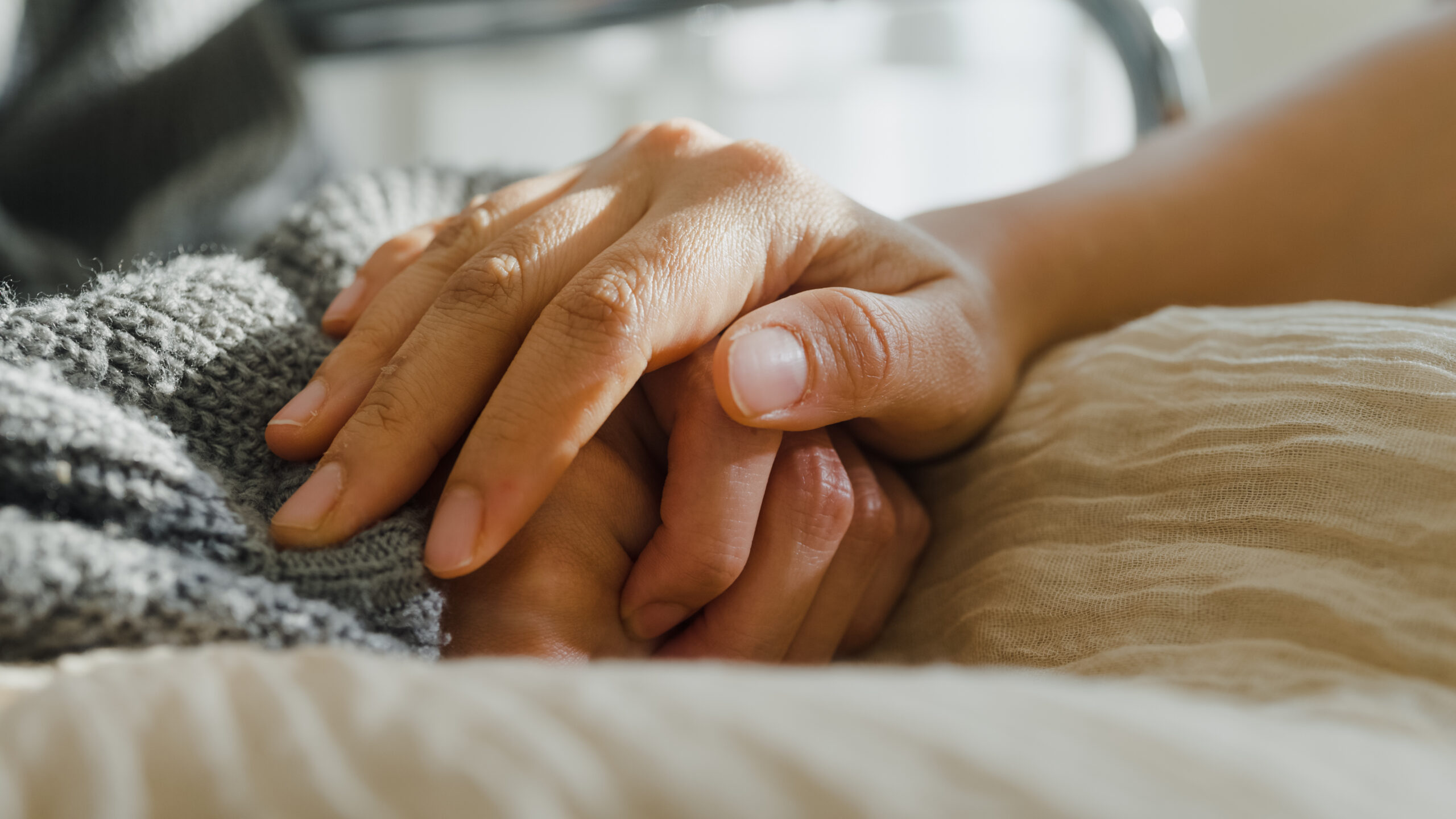 Hands clasped together on a blanket, offering comfort