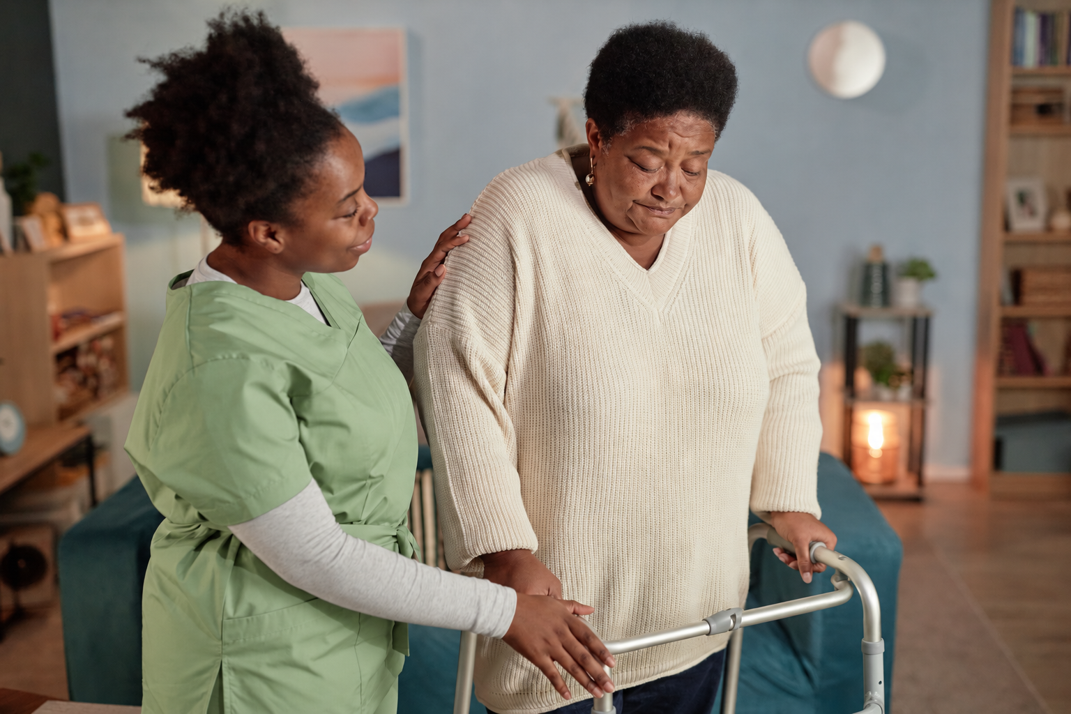 Carer helping an older woman walk with a walking frame at home