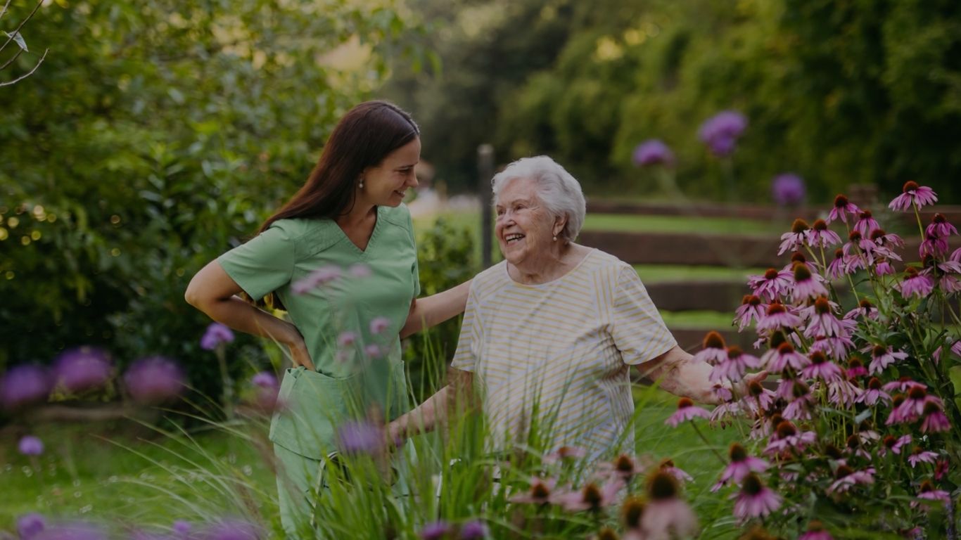 Carer and older woman walking together in a flower garden