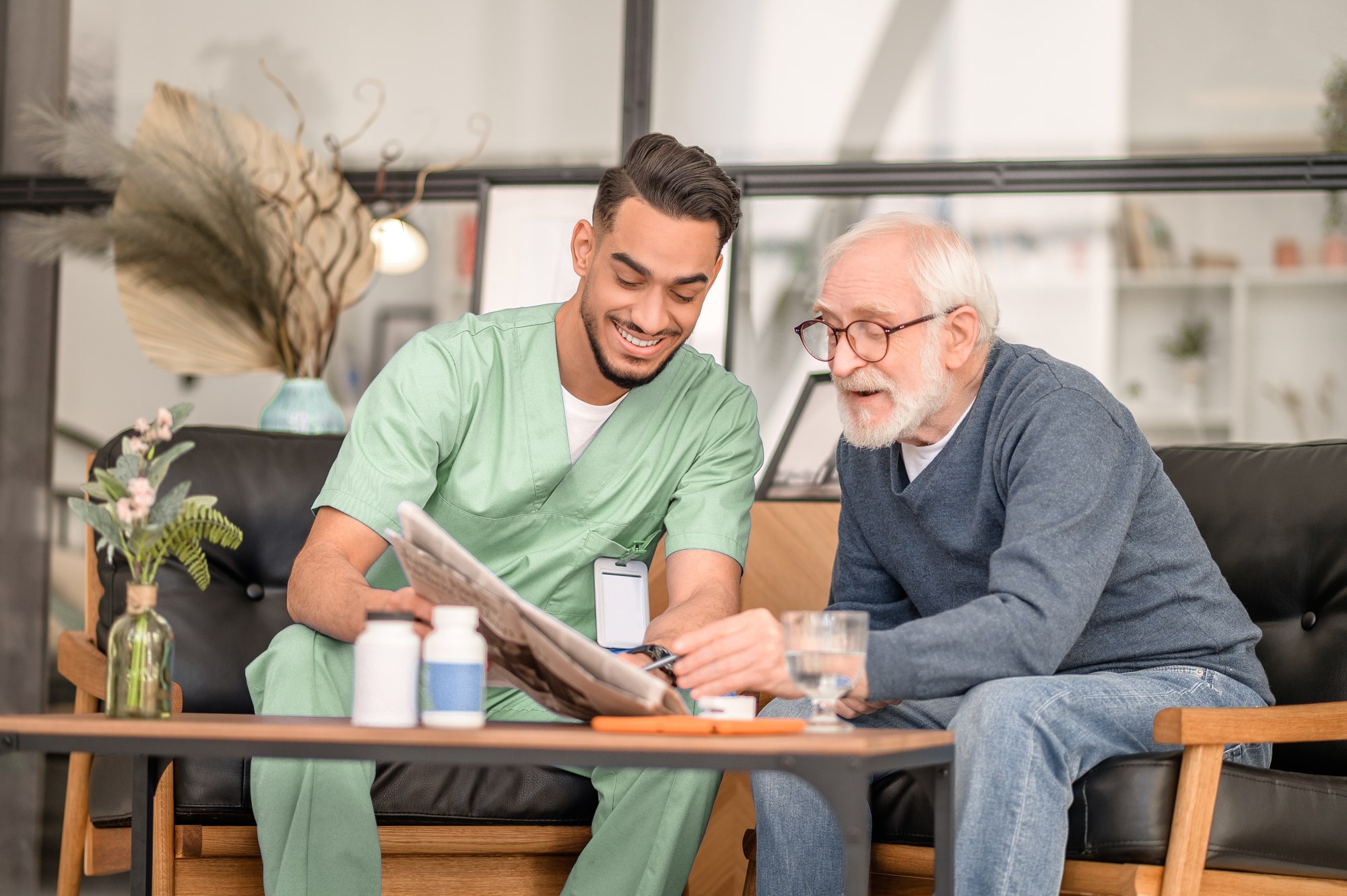 Carer sitting with an older man at home, helping him with his medication